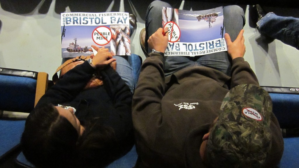 Two activists hold anti-Pebble Mine posters in a back row of the Wendy Williamson Auditorium during an EPA public comment meeting on the Draft Bristol Bay Watershed Assessment.