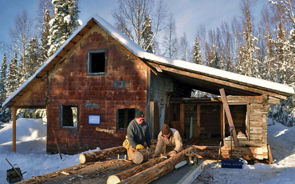 Volunteers Bill Nelson (left) and Bud Crawford unload logs in front of the Watchmen's Cabin, which is being restored at the Kasilof Regional Historical Association's museum. Photo courtesy Joseph Robertia, Redoubt Reporter. 