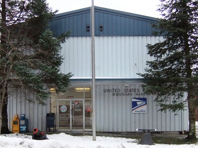 A blue USPS building with two spruce trees on either  side.  