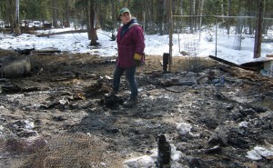 Brandy McLean walks through the rubble where the barn that burned down last week once stood, as one of the Large Black Hogs she's raising lounges nearby, left. Photo by Tim Ellis, KUAC - Fairbanks