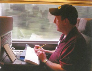 Gurney works while observing the scene out the window of a train.