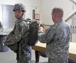 A soldier and jump master demonstrate how to put on a parachute. Photo by Josh Edge, APRN - Anchorage.