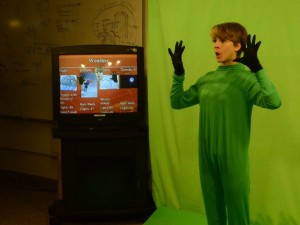 Freshman Jessie Gregg tests a green screen effect for the Halloween episode of JDTV News. The monitor shows what viewers are supposed to see. (Photo by Jeremy Hsieh/ KTOO)