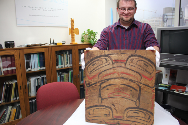 Archivist and collection manager for Sealaska Heritage Institute Zachary Jones holds up the wood panel, which arrived last week. (Photo by Lisa Phu/KTOO)