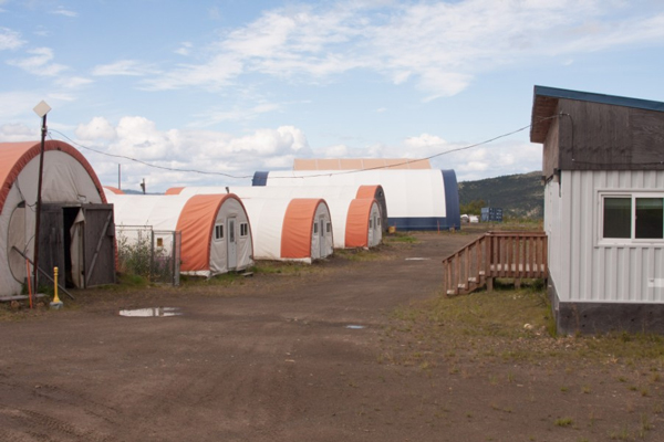 three white quonset huts sit on a dirt road