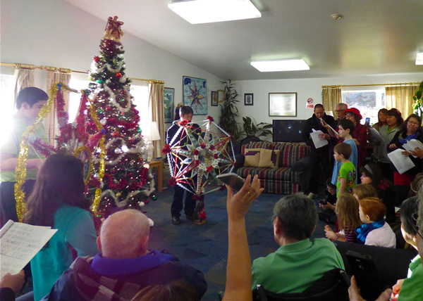 The congregation and other Unalaskans gather for a starring at Unalaska's senior center. At far right, Father Evon Bereskin joins in the caroling.  (Photo by Annie Ropeik, KUCB - Unalaska)
