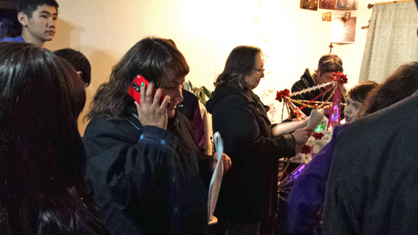 Marie Schliebe, left, calls a friend to let them listen in on a home starring. At right, Sharon Svarny Livingston looks over her packet of Russian carol lyrics. (Photo by Annie Ropeik, KUCB - Unalaska)