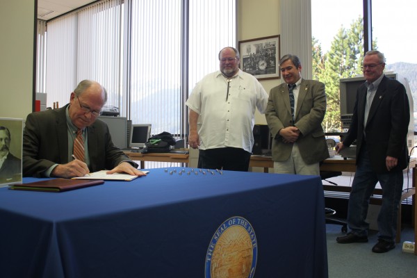 Gov. Bill Walker signs the bill Tuesday morning as Juneau Mayor Merrill Sanford, Rep. Sam Kito III and Sen. Dennis Egan look on. (Photo by Lisa Phu/KTOO)