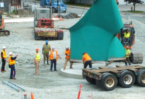 Sculptor Robert Murray (second from left) directs construction workers on the placement of Nimbus at the Father Andrew P. Kashevaroff State Library, Archives, and Museum on Saturday. The sculpture was lifted off the trailer and lowered into place by the excavator behind it. (Photo by Matt Miller/KTOO)