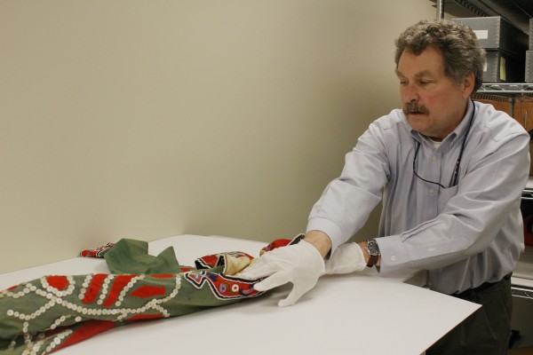 Chuck Smythe unrolls the tunic from storage. It’s kept this way to avoid damage. (Photo by Elizabeth Jenkins/KTOO)