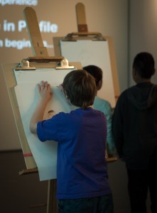 Middle schoolers try there hands at sketching portraits in profile, guided a short video. The easels will be up for the remainder of the exhibit. (Photo: Zachariah Hughes, KSKA)