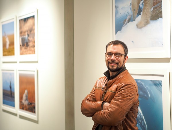 Florian Schulz standing in front of several works, including the exhibits lead image, a polar bear gnawing on the spine of a Fin Whale. To get the shot, Schulz set a camera near the carcass, snapping photos with a remote from 50 yards away. (Photo: Zachariah Hughes, KSKA)