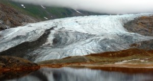 A glacier reflects in a naturally occurring pool of rusty, acidic water at the site of one of the KSM prospect’s planned open-pit mines. (Photo by Ed Schoenfeld/ CoastAlaska News).