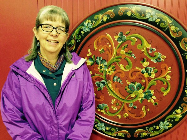 Jill Williams stands with a traditional Norwegian rose mauling design piece inside the Sons of Norway Hall. Photo/Angela Denning