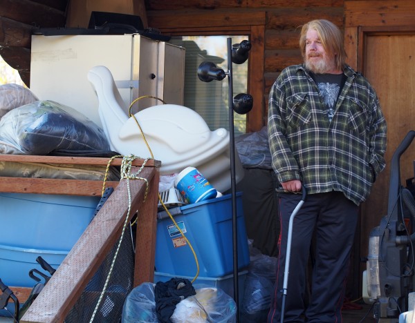 Scott Harrison standing outside the cabin he rents in Big Lake. It's too small inside for him to fit many of his possessions, so he keeps more durable items like clothes and dry-goods outside. Photo: Zachariah Hughes, KSKA