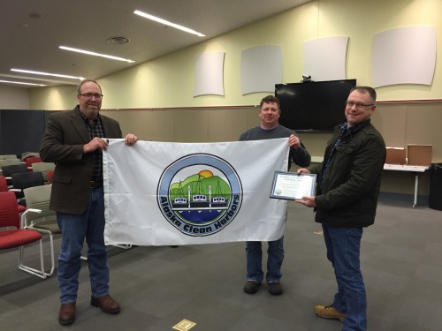 From L to R: Chuck Hackett, Brett Farrell, and Stan Eliason hold the flag, designating Sitka as an “Alaskan Clean Harbor.” (Emily Kwong/KCAW photo)