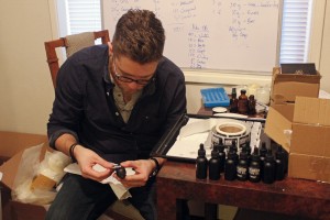 Steven Cornfield puts new labels on the new batch of beard oil. (Photo by Josh Edge/APRN)