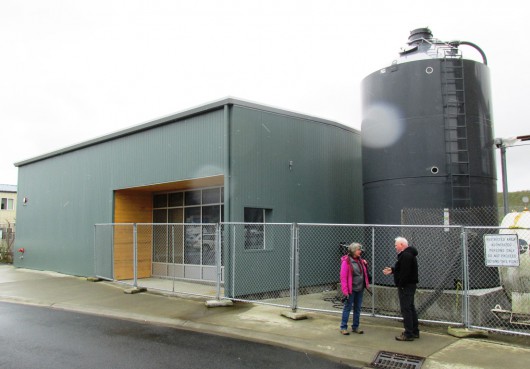 Karen Petersen and Mike Carney talk outside the Ketchikan International Airport’s new biomass boiler building. The pellet silo on the right holds up to 30 tons. (Photo by Leila Kheiry, KRBD - Ketchikan)