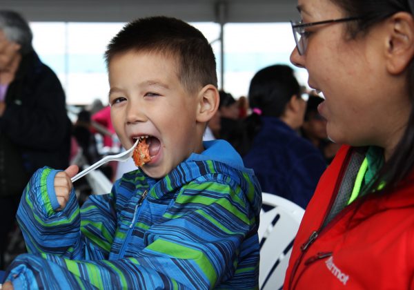 Kacin Byayuk enjoys a forkful of salmon while mom Diana Gamechuk looks on at a community cookout hosted by the Bristol Bay Native Corporation celebrating Salmon Day in Anchorage on August 10. (Photo by Graelyn Brashear - KSKA/Anchorage)