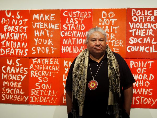 Artist Edgar Heap of Birds stands before his piece "Dead Indian Stories" on display in the "Without Boundaries" exhibit. (Photo: Zachariah Hughes, Alaska Public Media - Anchorage)
