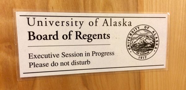A white sign on a light wooden door says  "University of Alaska Board of Regents/Executive Session in Progress/Please do not disturb"