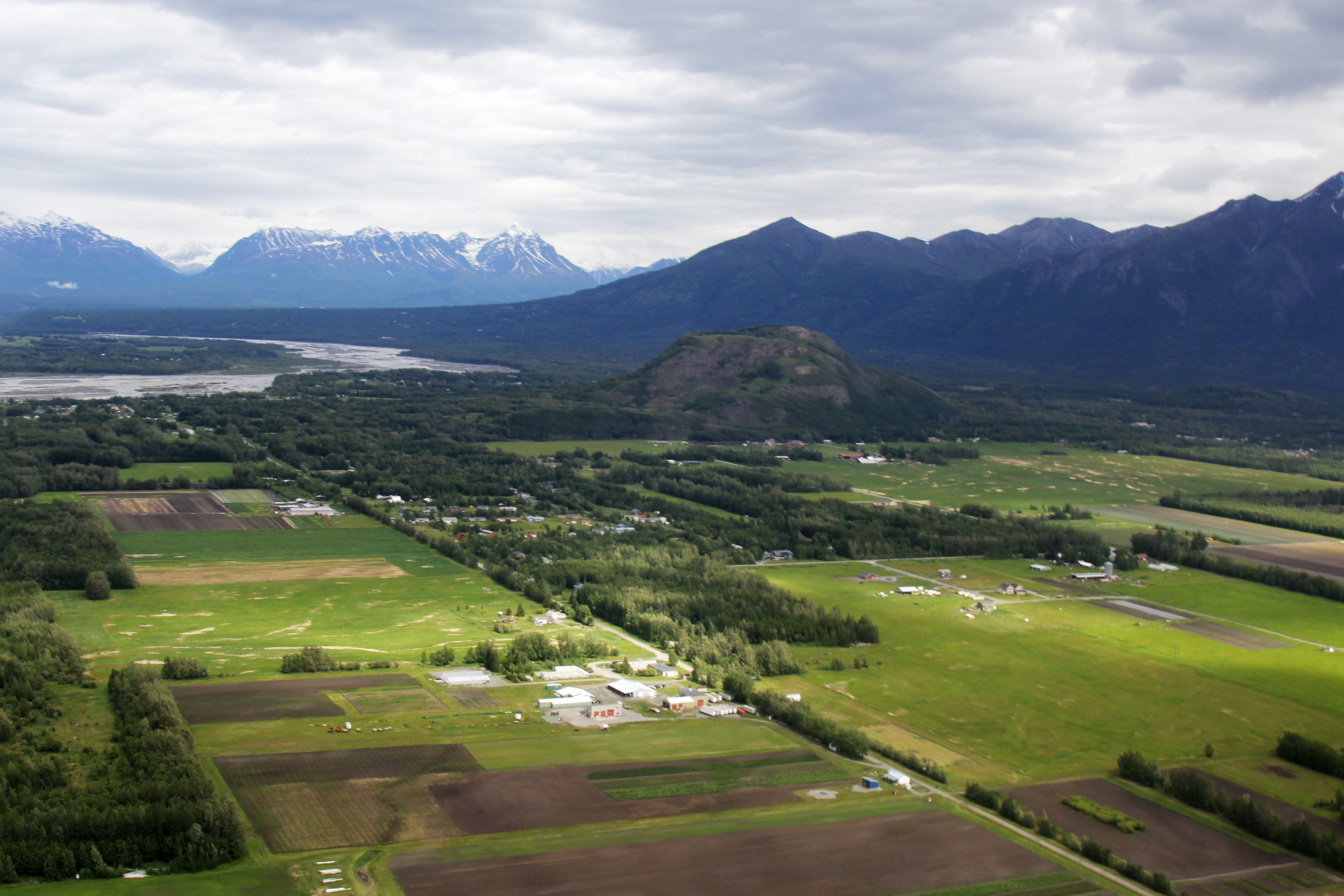 An aerial view of green farmland with a mountainous backdrop.