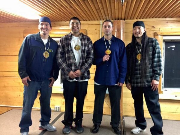 Four Alaska Native men stand in a log room