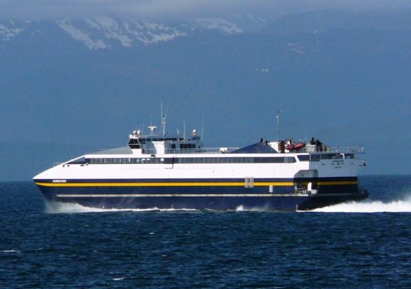 A blue and white ferry travels through the water on a clear day with mountains in the background