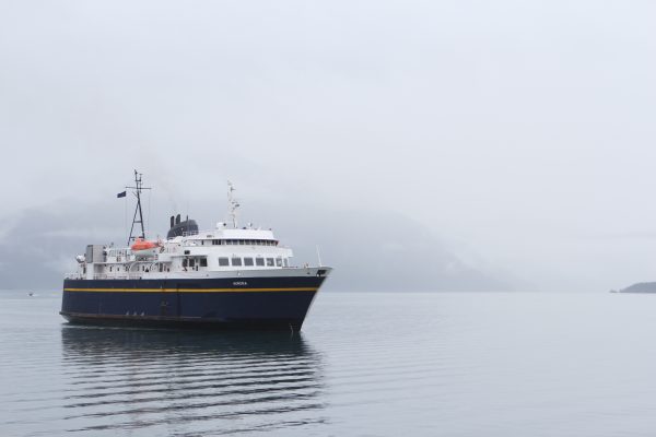 A blue and white ferry in the left hand side of the image sails in foggy weather and a foggy mountain in the background 