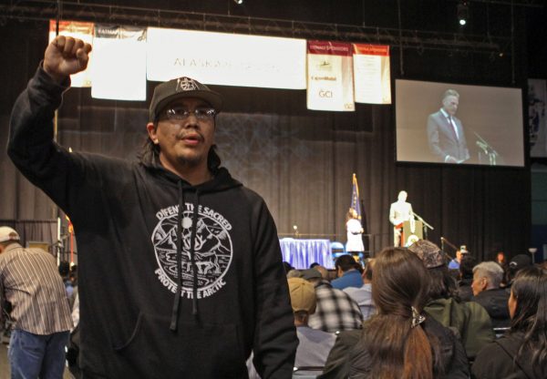 An Alaska Native man in a black sweatshirt stands and speaks