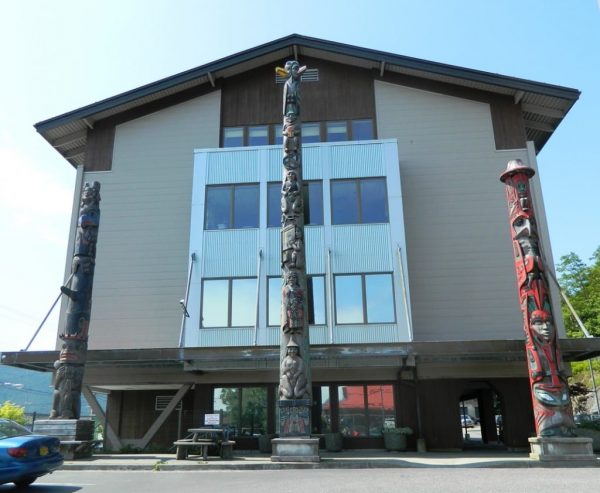 Totem poles stand in front of a beige building