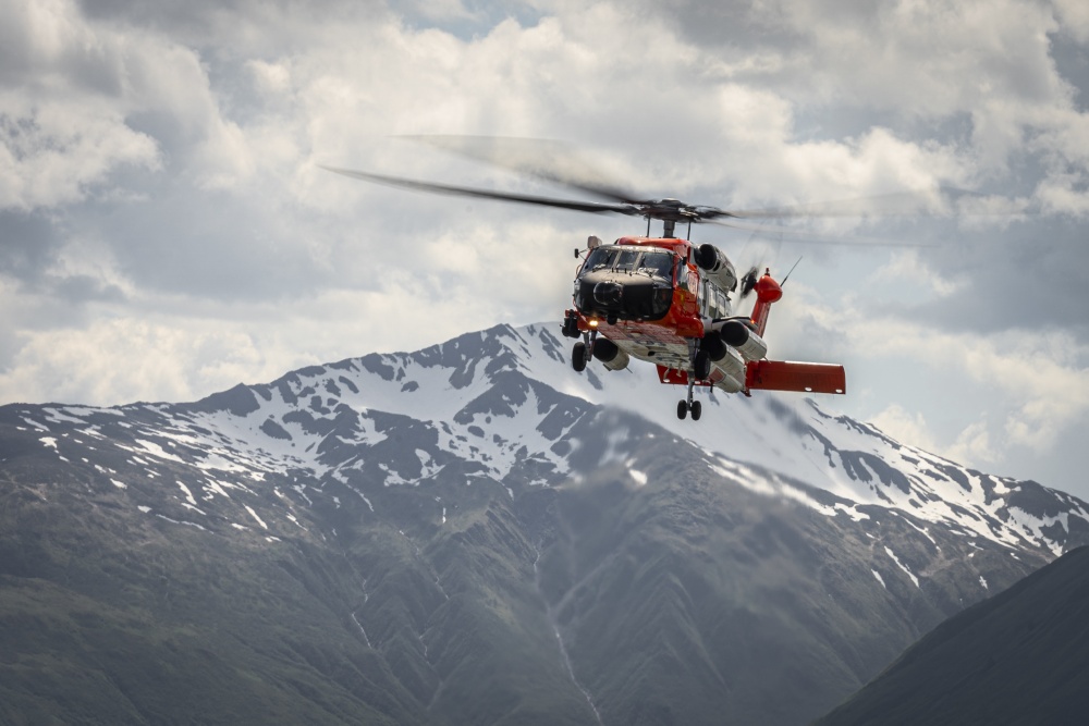 A orange and white helicopter flies in front of a mountain