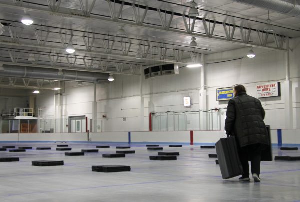 A worker lays out mats in an ice rink under bright flood lights.