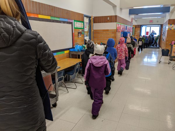 A line of elementary children line up and walk down the hallway out to recess in the winter