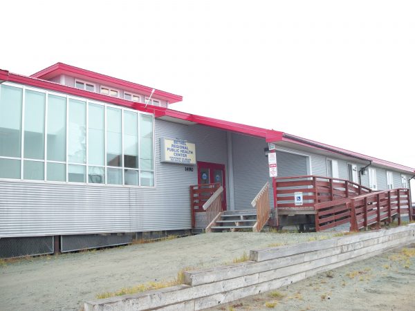 A grey building with a red roof and wooden stairs leading ip next to a boardwalk