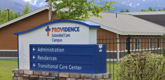 A blue sign with directions that says "Providence Extended Care" and has a house in the background.