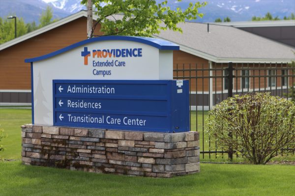 A blue sign with directions that says "Providence Extended Care" and has a house in the background.  