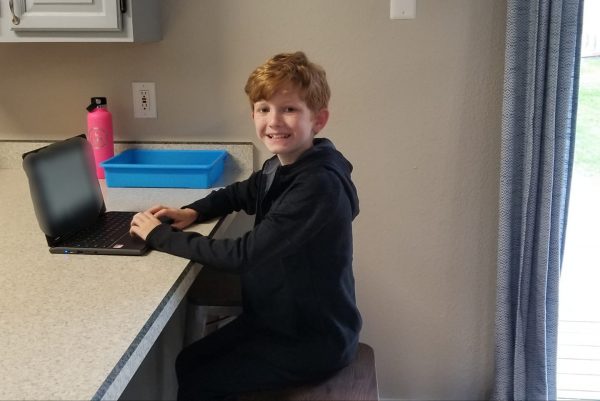 A young boy sits at a countertop with his laptop
