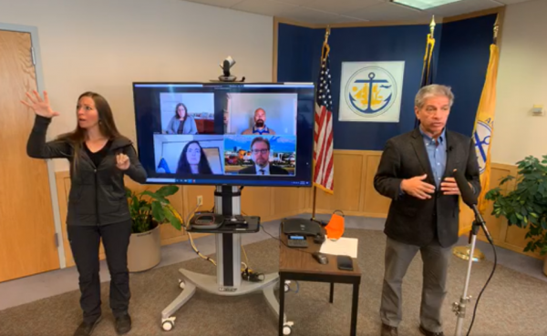 A ASL interpreter signs on the left, a screen with four faces in the middle, and Berkowitz on the right. 