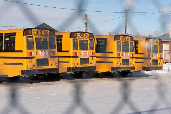 Yellow school buses as seen through a chain link fence in snow-covered ground