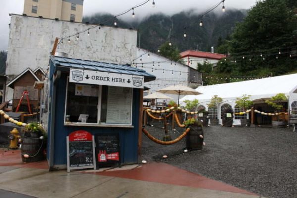 A small blue food stand in an open outdoor gravel-laden food court with a sign that says "order here" above the window.