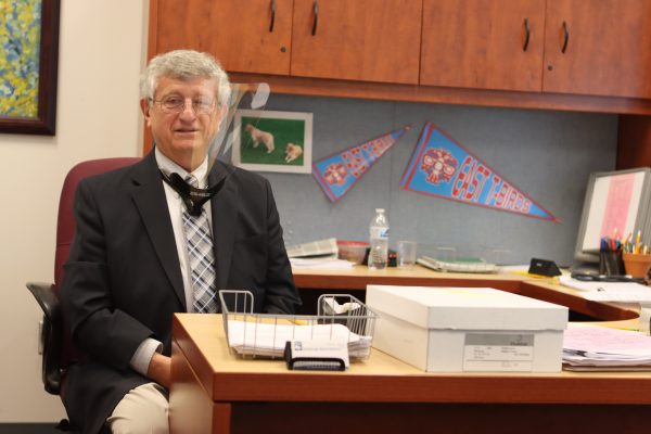 East High School Principal Sam Spinella sits behind his desk wearing a face shield.