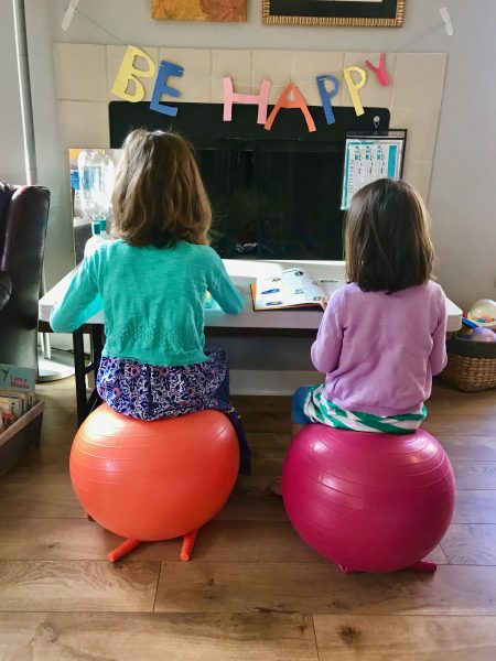 Two girls sit on inflatable balls while working on laptops
