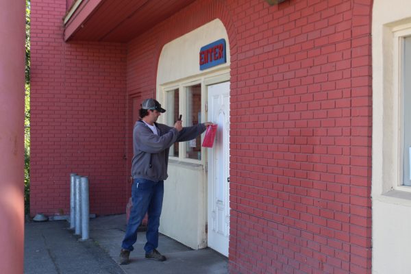 A man in a sweatshirt and baseball cap pulls a red stop work order sign from the white door of Kriner's Diner, as he takes a video of his himself removing the sign with his cell phone.