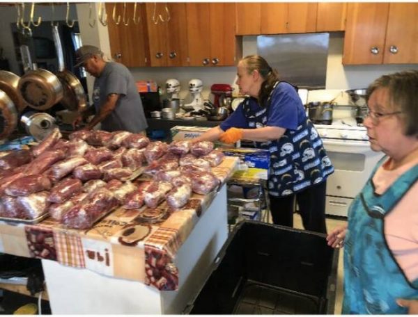 Several Alaska Natives work on processing meat in a kitchen.