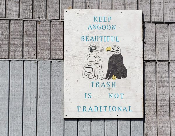 A white sign on a wall says "Trash isn't traditional/Keep Angoon beautiful)