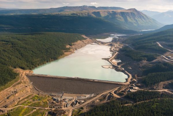 An aerial shot of a massive dam holding in mine tailings surrounded by spruce forests and rolling hills. 