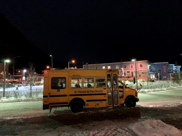A yellow shuttle waits in a snowy parking lot