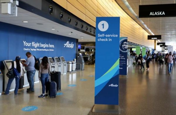 Passengers check in at one of about a half dozen kiosks next to blue Alaska Air banners