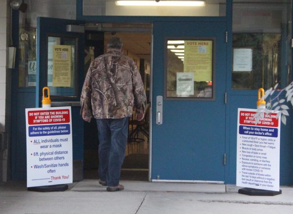 A man in a camoflauge jacket and jeans walks through blue doors with notices about health warnings